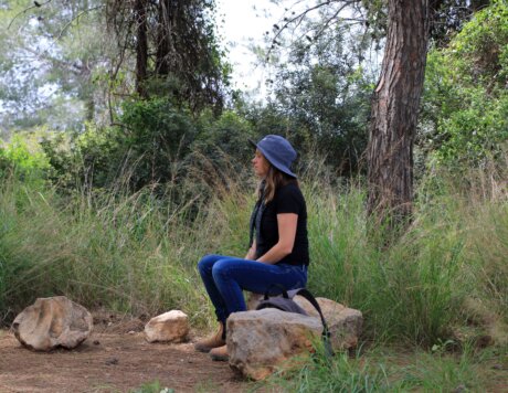 בחורה עם כובע יושבת על סלע באמצע הפארק, מוקפת בעצים ושקט